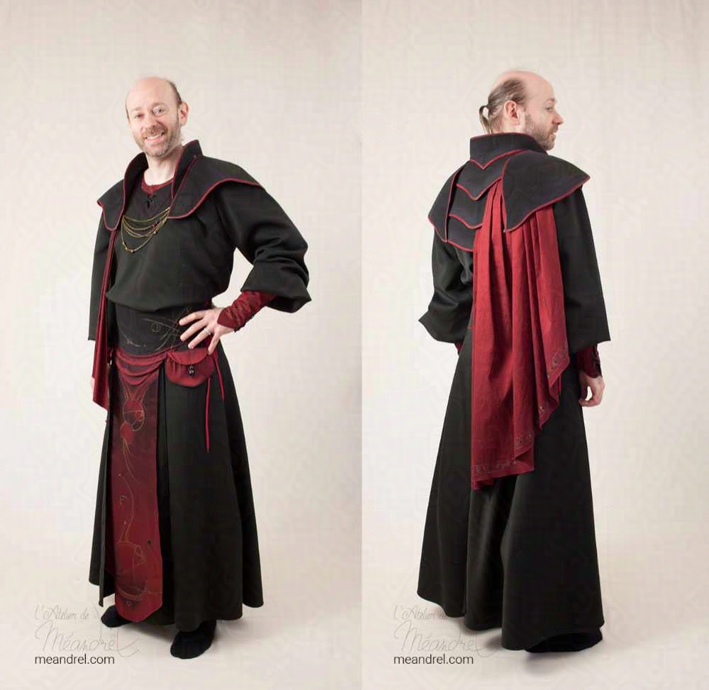 Photo de face et dos du costume précédent, en pied cette fois : tenue noire et rouge, avec jupe longue et tunique, large ceinture à pan central, et pièce d'armure en haut d'où part une cape plissée.