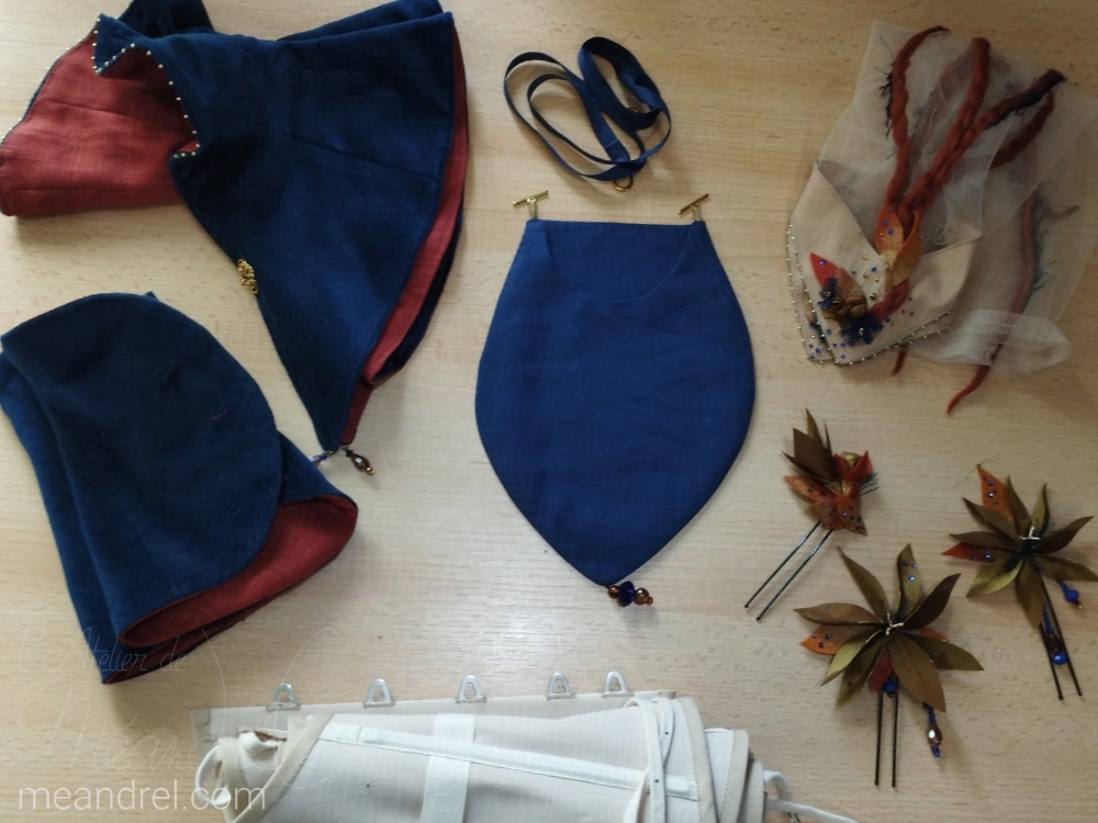 Photos sur une table des accessoires : les épingles à cheveux, le sac, les manchettes, un serre-taille roulé, et des sur-manchettes et un col en velours.