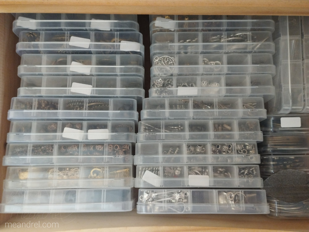 Un tiroir plein de boites à compartiments dont certains portent une petite étiquette blanche.