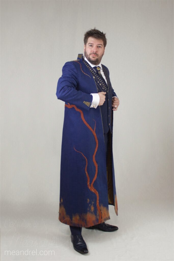 Photo en pied du même manteau long, où on voit la liane qui grimpe depuis le bas jusque dans le dos, en passant sous le bras.