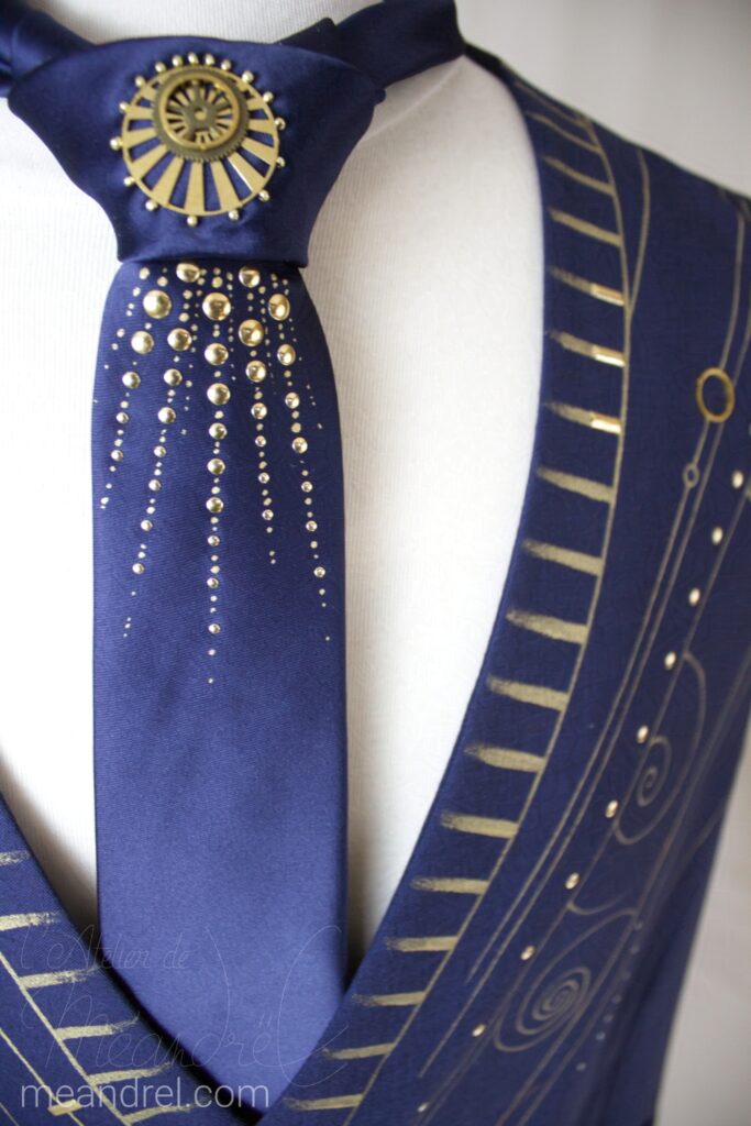 Photo de l'encolure du gilet avec des motifs dorés peints, et de la cravate bleue à décorations rayonnantes or.