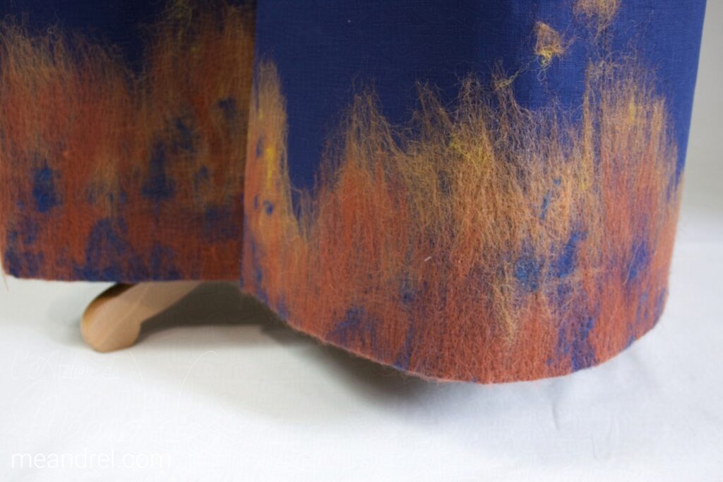 Photo de détail de la laine feutrée du bas du manteau, formant des nuances de roux et orangés.