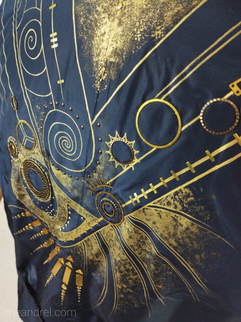 Photo du dos du gilet, où on voit les décorations dorées : grandes lignes en V, cercles, spirales, petits points, lignes barrées...