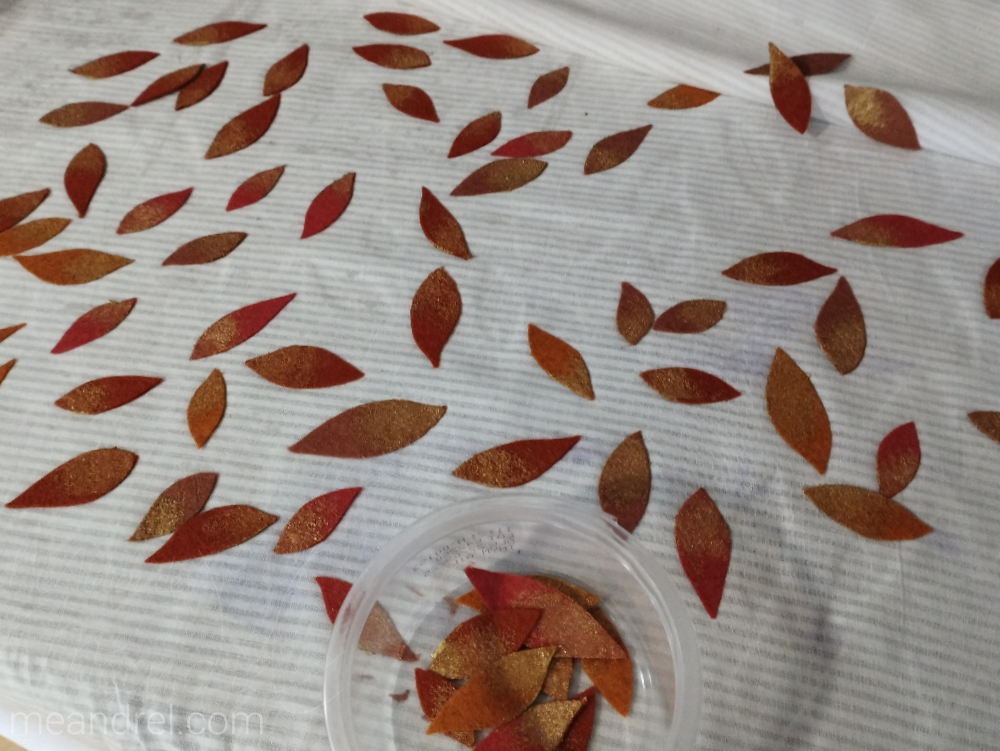 Petites feuilles en cours de peinture (dégradé or) sur une table.