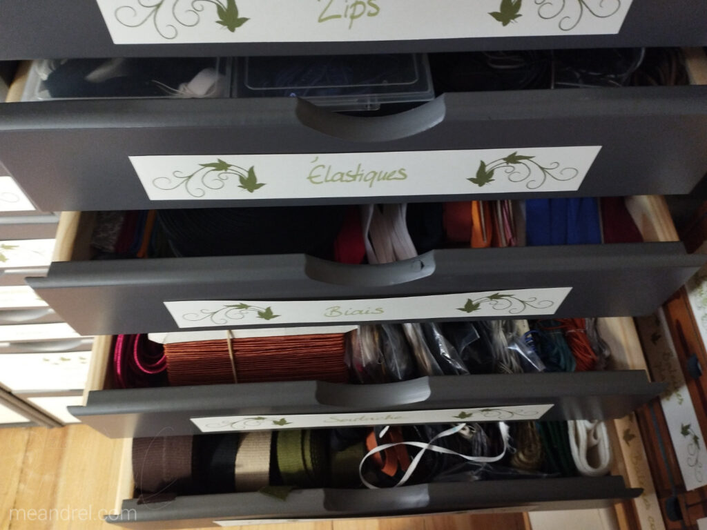 Des tiroirs entrouverts, on lit "zips", "élastiques", "biais", et on aperçoit le contenu.