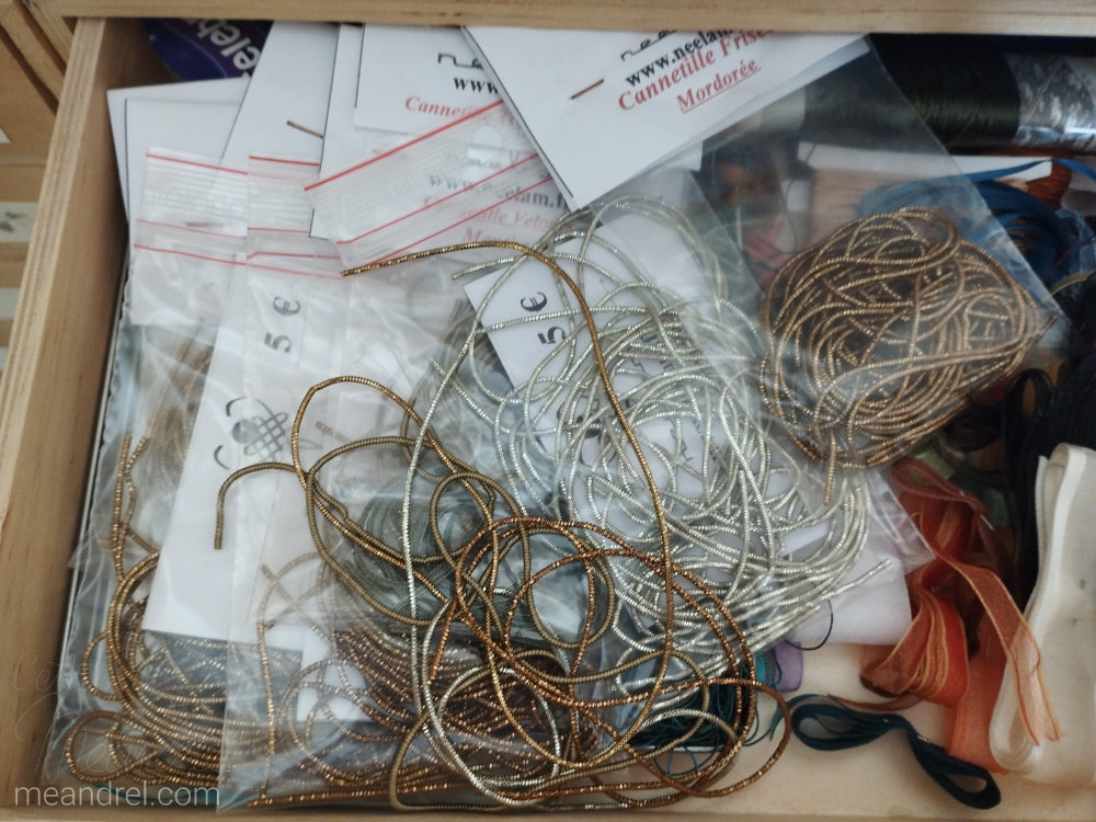 Tiroir vu du dessus, plein de sachets de "fil" de métal or et argent.