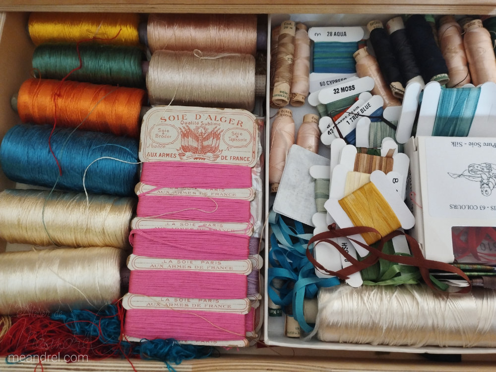 Tiroir vu du dessus, plein de rouleaux et cartons de fils soyeux et chamarés.