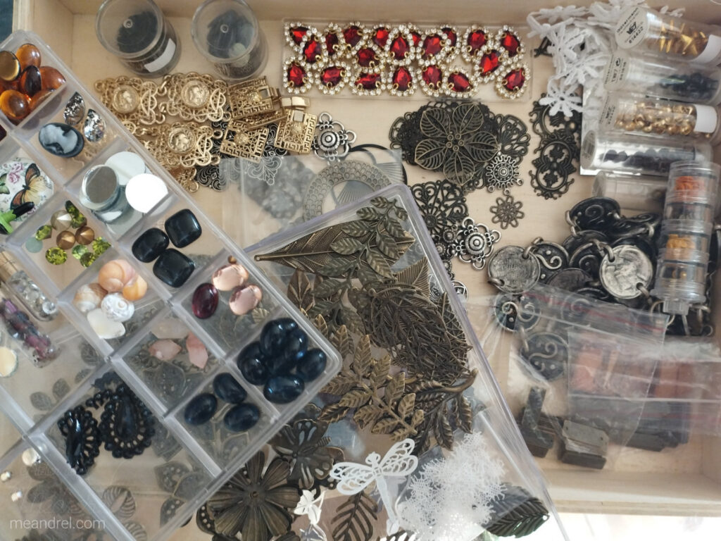 Tiroir vu du dessus, plein de petits éléments métalliques et de pierres en verre.