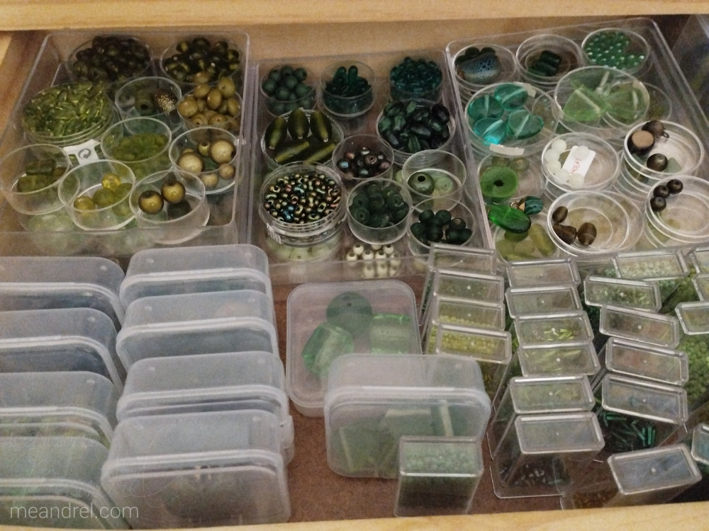 Tiroir vu du dessus, plein de boites rondes, rectangulaires et carrées pleines de perles.