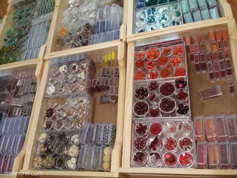 6 tiroirs vu du dessus, plein de perles rangées par couleurs et formes.