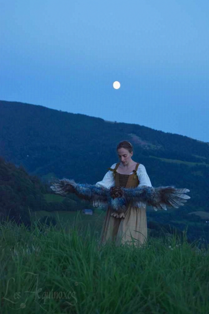 Une photo de la chouette portée par sa marionnettiste, au crépuscule, sur fond de collines bleues.