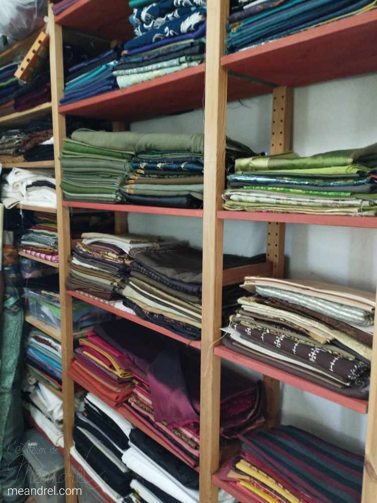 Des piles de tissus par couleur dans une étagère en bois.