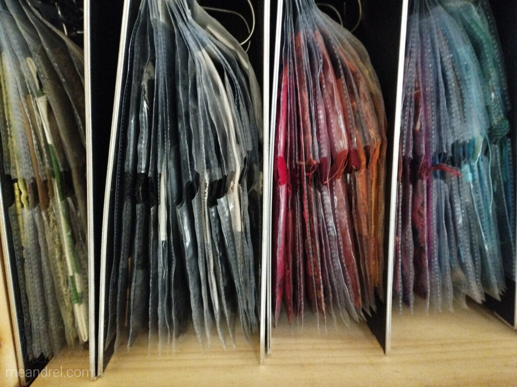 4 gros classeurs pleins de pochettes colorées dont on ne voit que la tranche.