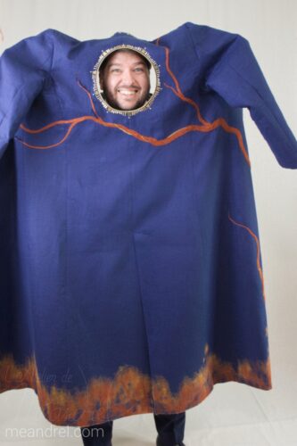 Photo du manteau tenu à bouts de bras, où le trou du dos sert de cadre photo : on ne voit que la tête de Sébastien par le trou !